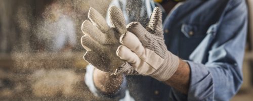 Close up of dusty work gloves Unrecognizable male hands with work gloves on, clapping to remove sawdust
